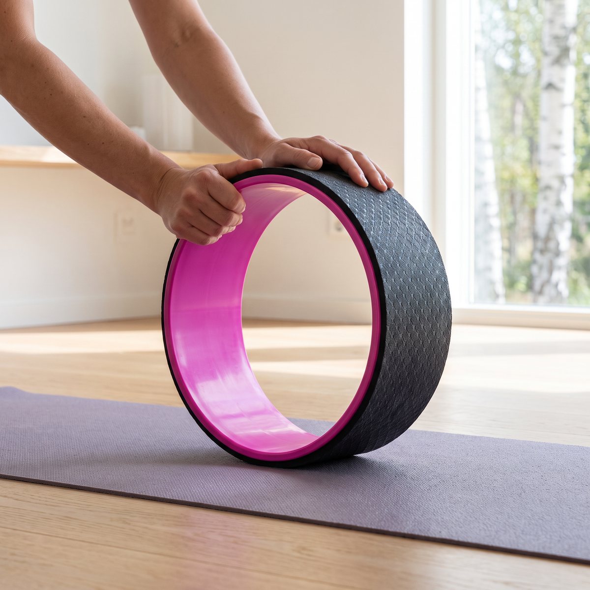 Svart yogahjul i TPE med rosa insida som rullas på en yogamatta i ett ljust svenskt hem med björkar utanför fönstret