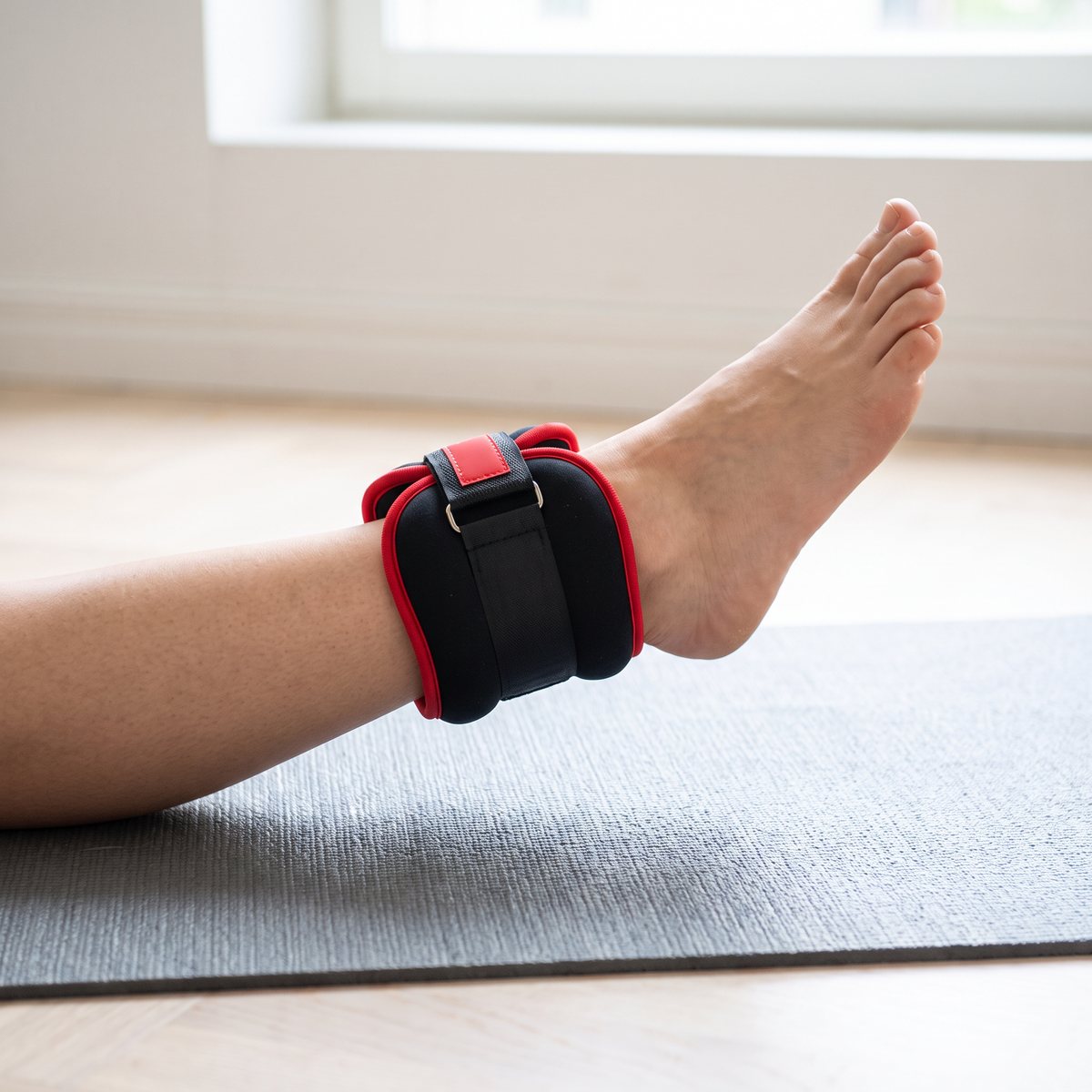 Gymsticks svarta manschett med röd kant runt en fotled vid golvövning på träningsmatta i ett svenskt hem