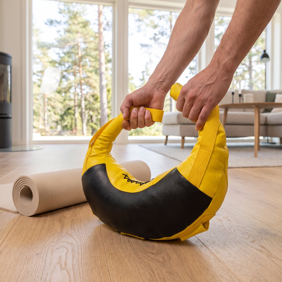 Gul och svart Tunturi Bulgarian Bag lyfts i remmarna på ett trägolv i ett ljust svenskt vardagsrum