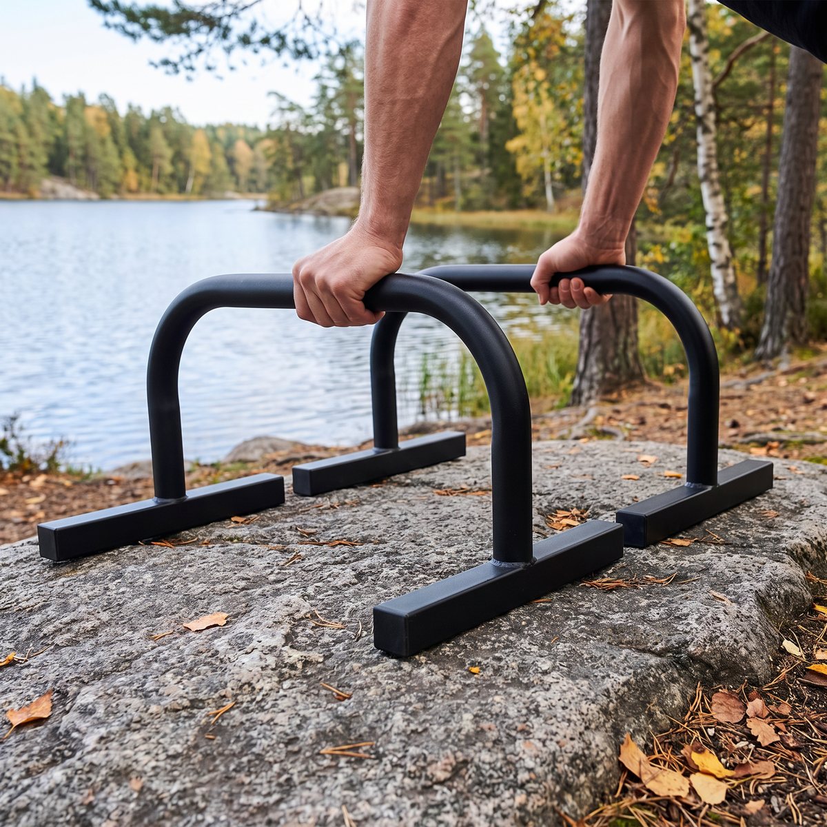 Svarta parallettes från Titan Life på en granithäll vid en svensk sjö bland tallar, händerna greppar stängerna