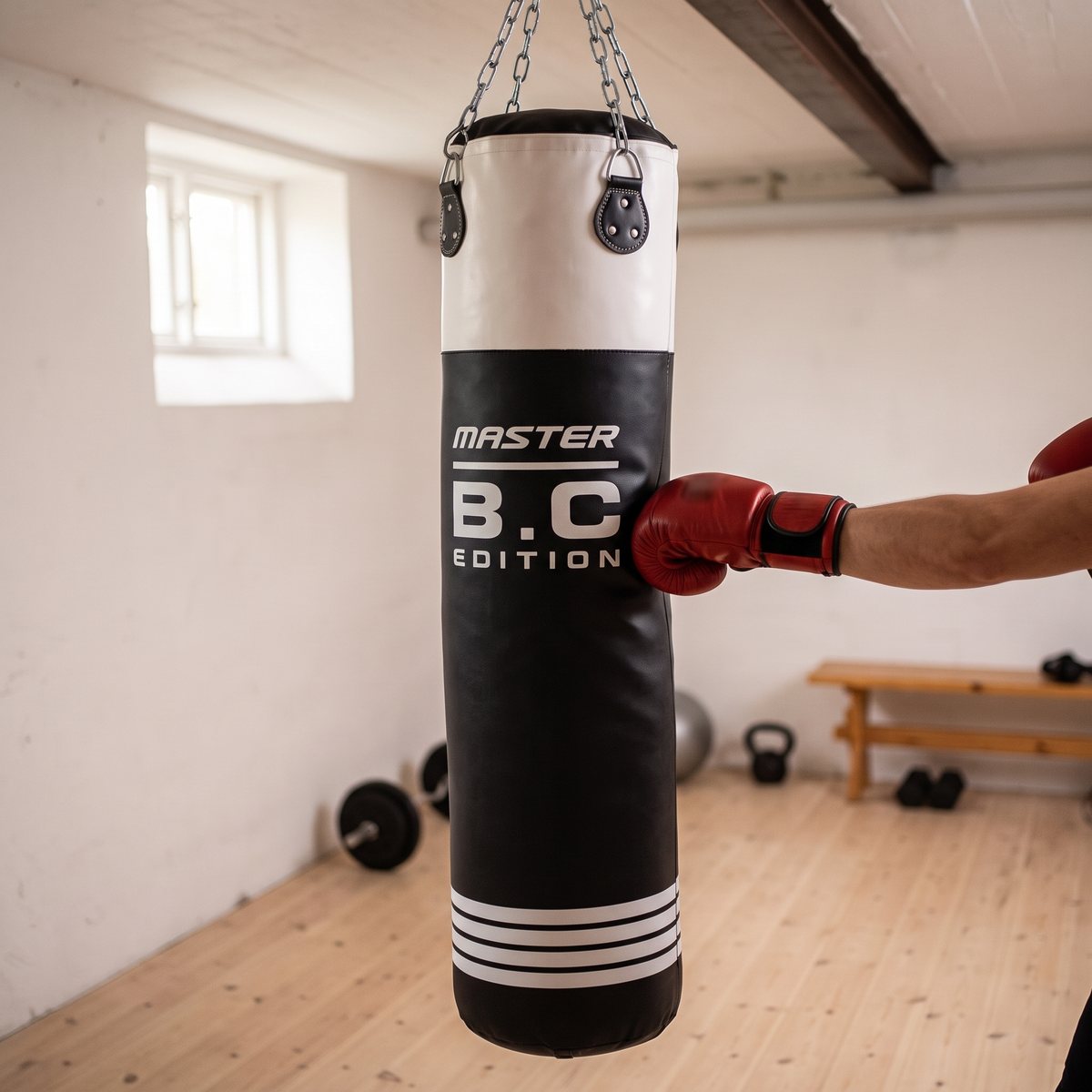 Svart och vit boxningssäck på kedjor som träffas av en röd boxningshandske i ett svenskt hemmagym i källaren