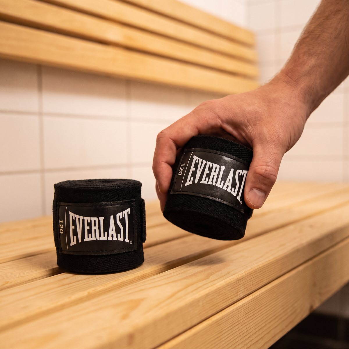 Svarta Everlast Core-handlindor på en furubänk i ett svenskt omklädningsrum, en hand plockar upp en rulle