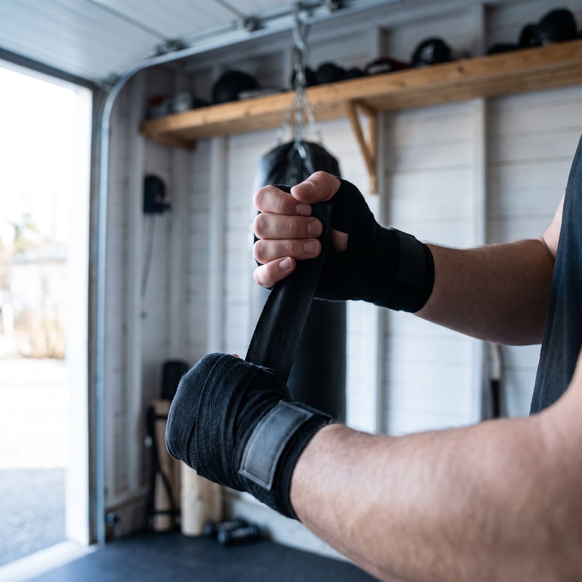 Person lindar handen med svart handlinda i ett svenskt garagegym med vita väggar och boxningssäck