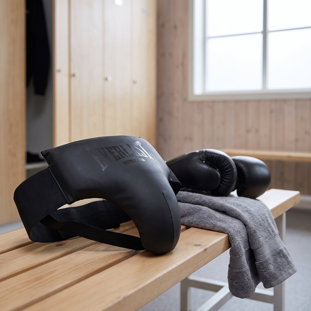 Svart Everlast Elite Suspensoar på en träbänk bredvid boxningshandskar och handduk i en svensk idrottshall