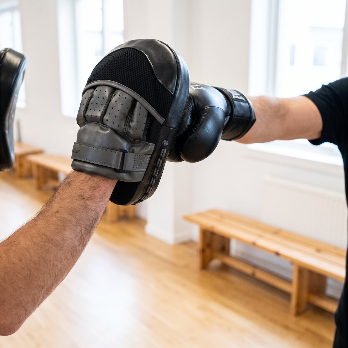 Tränare med Everlast Powerlock Mittsar på handen tar emot en rak slag från en boxare med handskar i en ljus svensk träningslokal med trägolv