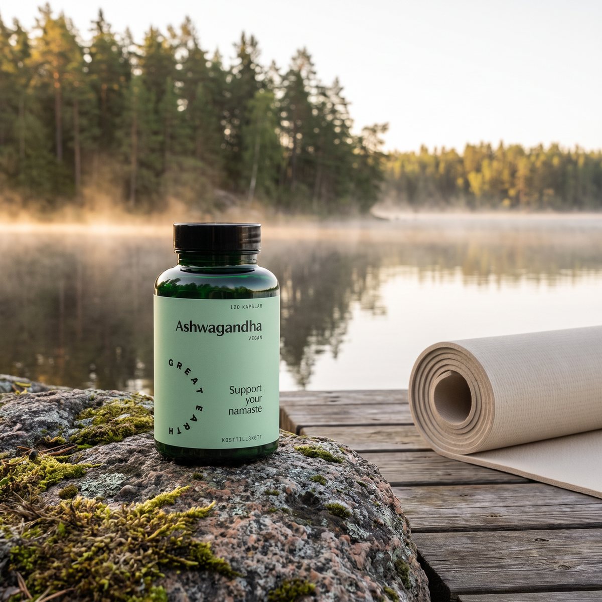 Burk med Great Earth Ashwagandha på en mossbeklädd granithäll vid en svensk sjö i gryningen, med en yogamatta på bryggan