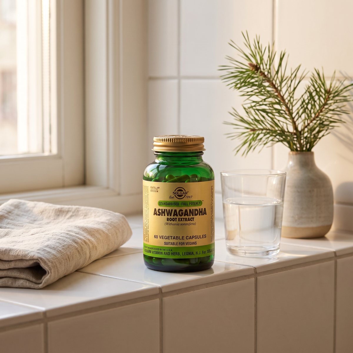 Burk med Solgar Ashwagandha på en kaklad hylla i ett svenskt badrum, med linnehandduk, vatten och en tallkvist