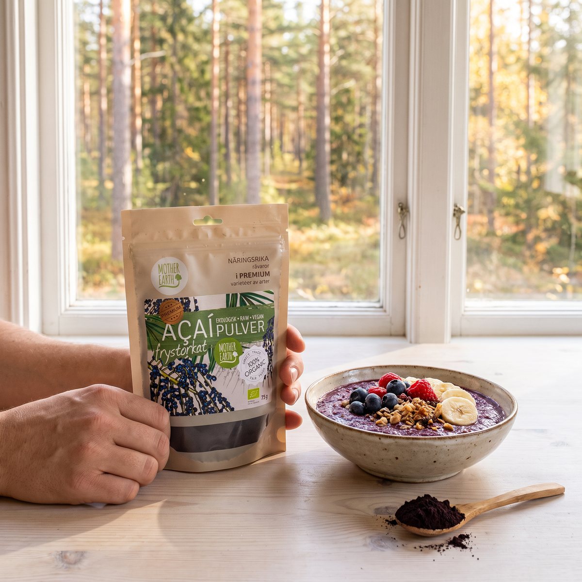Mother Earth acaipåse vid en skål med acaibowl på ett ljust bord framför ett fönster mot svensk tallskog