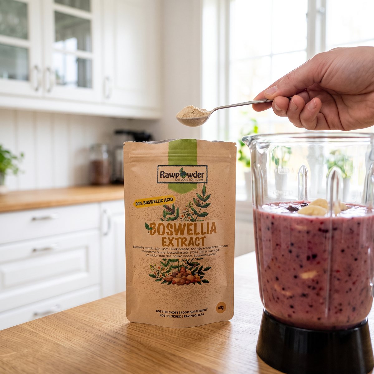 Rawpowder Boswellia extrakt-påse bredvid en mixer med smoothie i ett ljust svenskt kök, en hand håller en sked med pulver