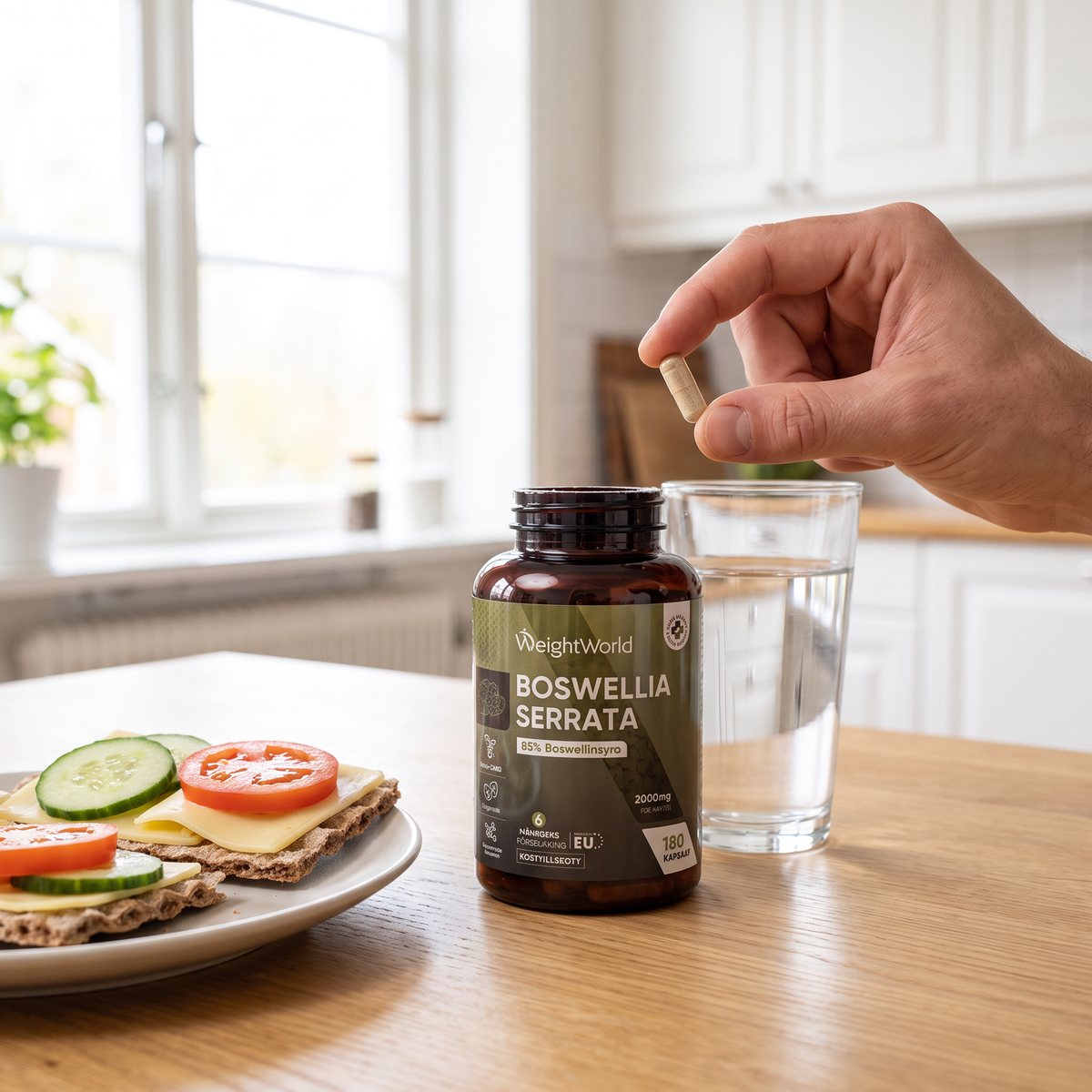 WeightWorld Boswellia Serrata 2000 mg-burk på ett ljust ektbord i ett svenskt kök med ett glas vatten och knäckebrödsmackor, en hand håller en kapsel