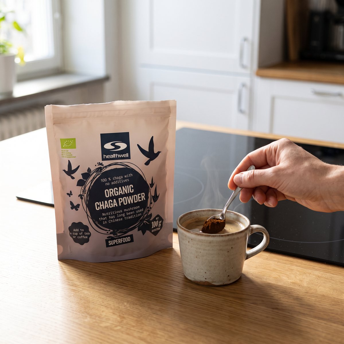 Healthwell Chaga EKO-påse på en köksbänk bredvid en kaffekopp med chagapulver, i ett svenskt kök