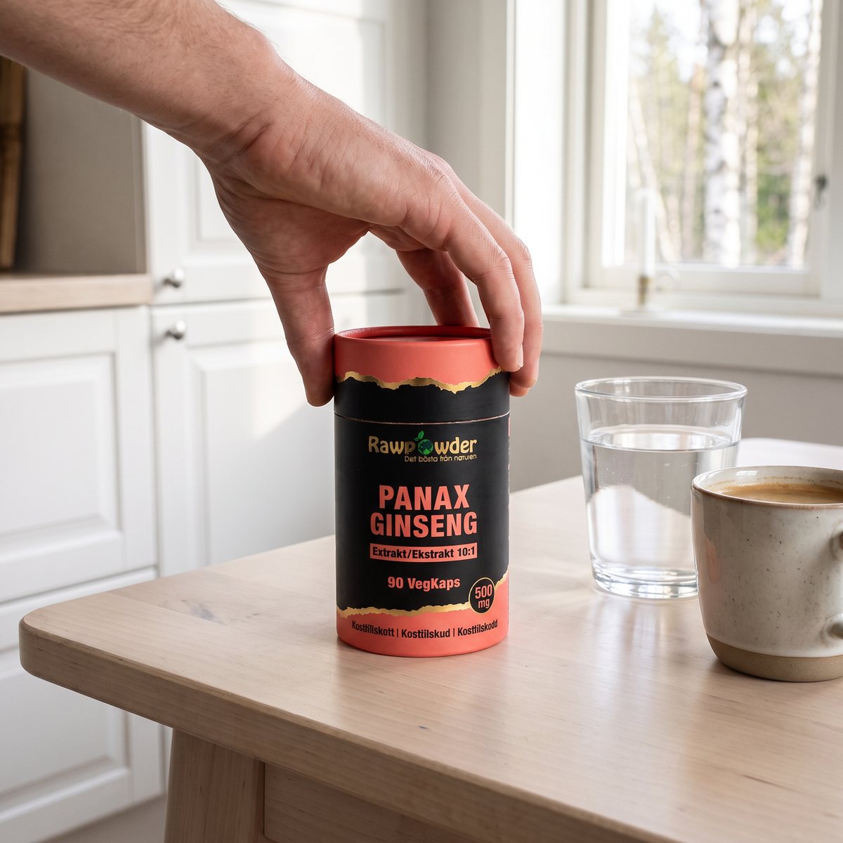 Rawpowder Panax Ginseng Extrakt i svart och korallröd burk på ett björkbord i ett svenskt kök, med vattenglas och kaffe
