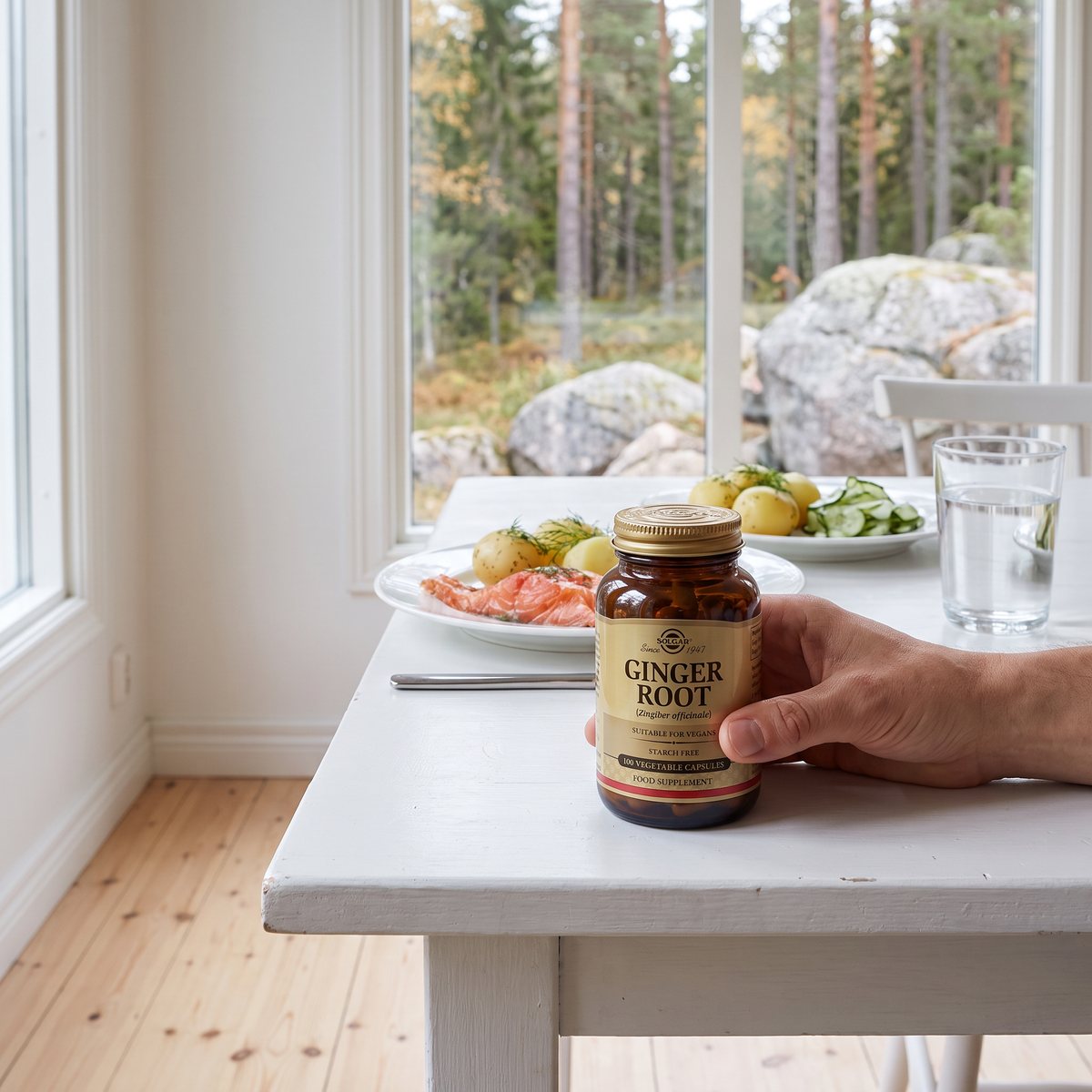 Brun glasburk Solgar Ginger Root på ett vitt matbord med lax och färskpotatis, tallskog och granithällar utanför fönstret