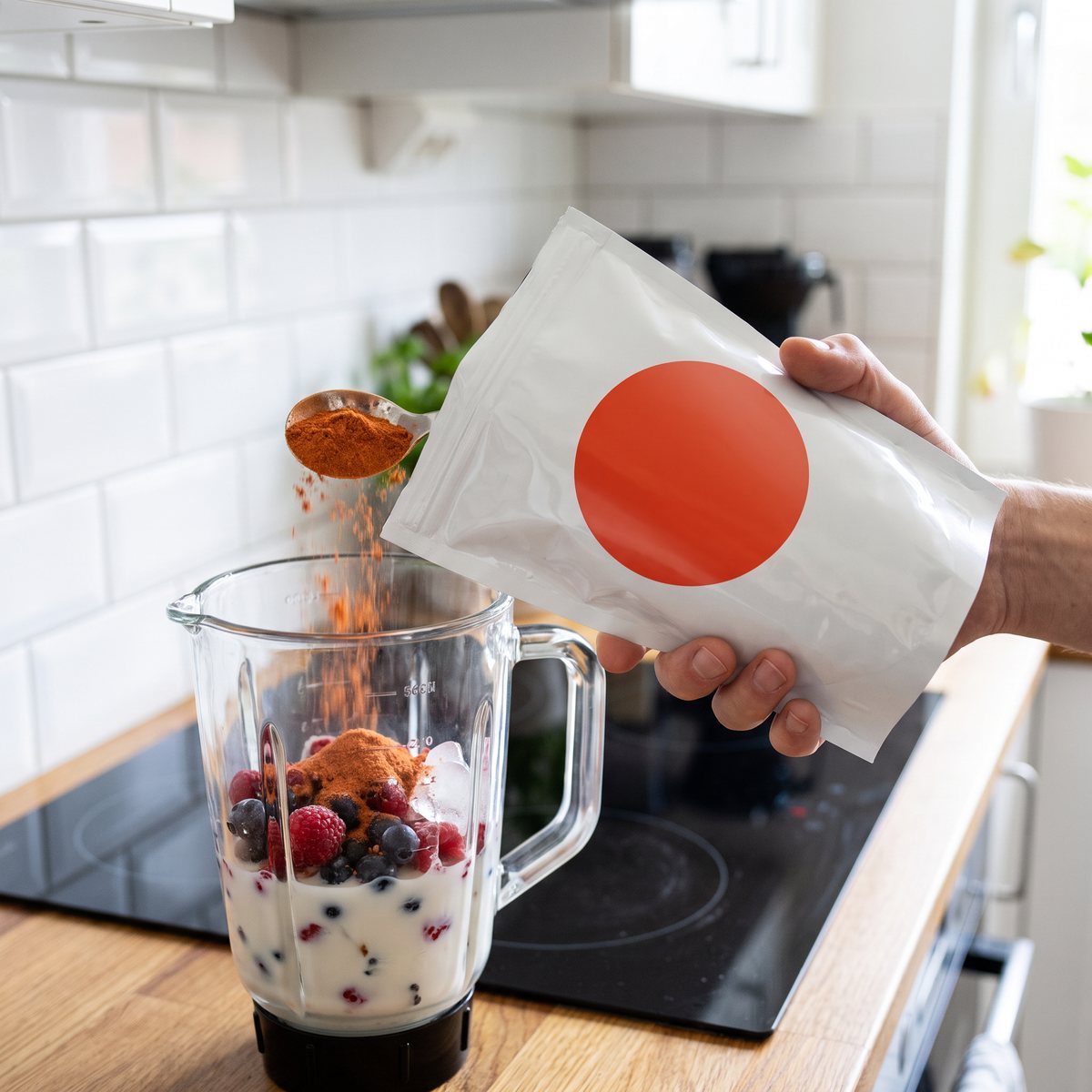 En hand som håller en vit påse med nyponpulver och tillsätter pulver i en mixer i ett svenskt kök