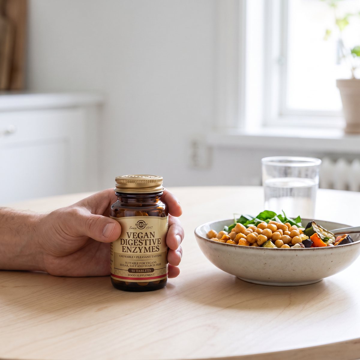 Solgar Vegan Digestive Enzymes i handen vid en vegetarisk lunchskål på ett björkbord i ett svenskt hem