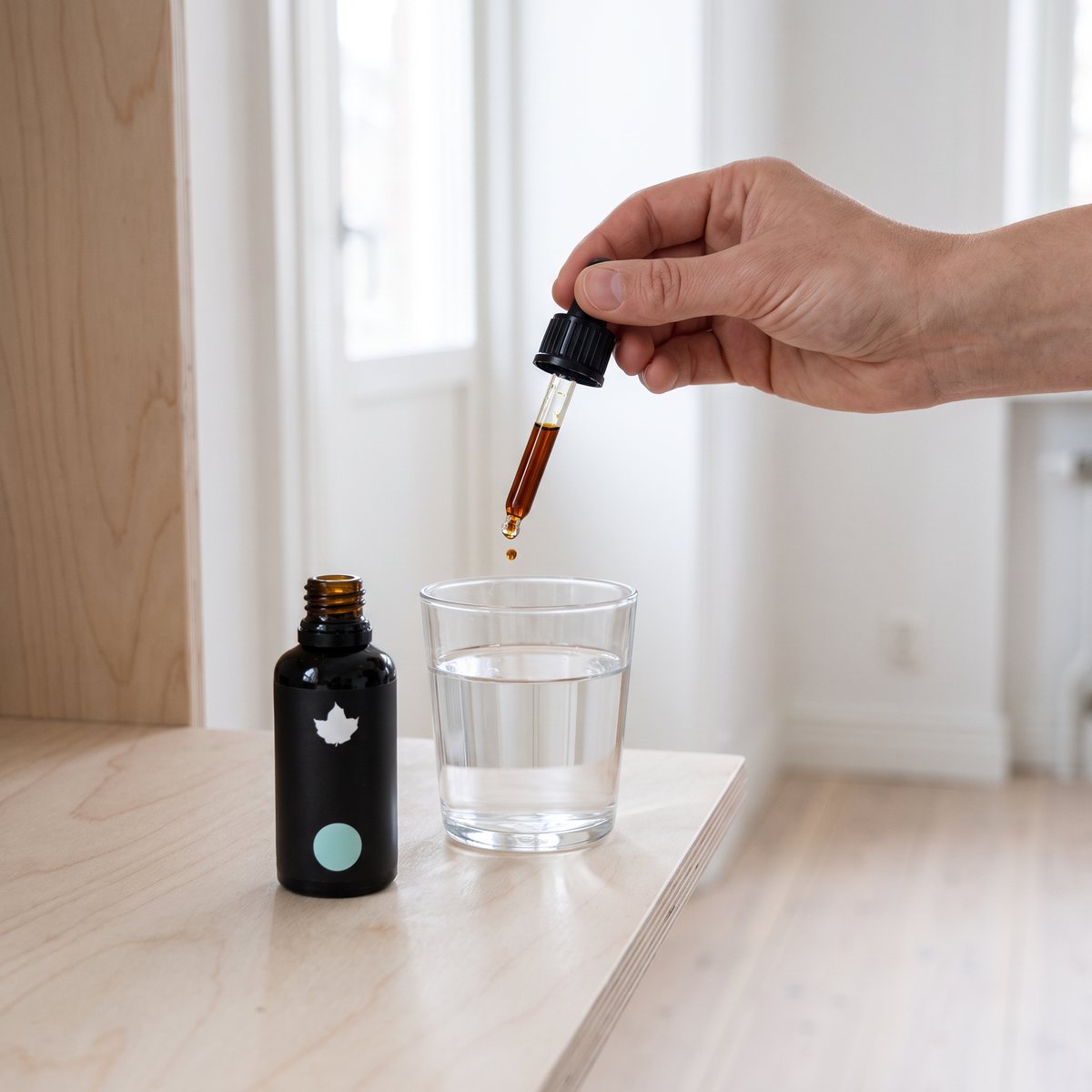 Svart droppflaska med Pureness Premium Research Reishiextrakt och en pipett som droppar i ett glas vatten på ett ljust träbord i ett svenskt hem