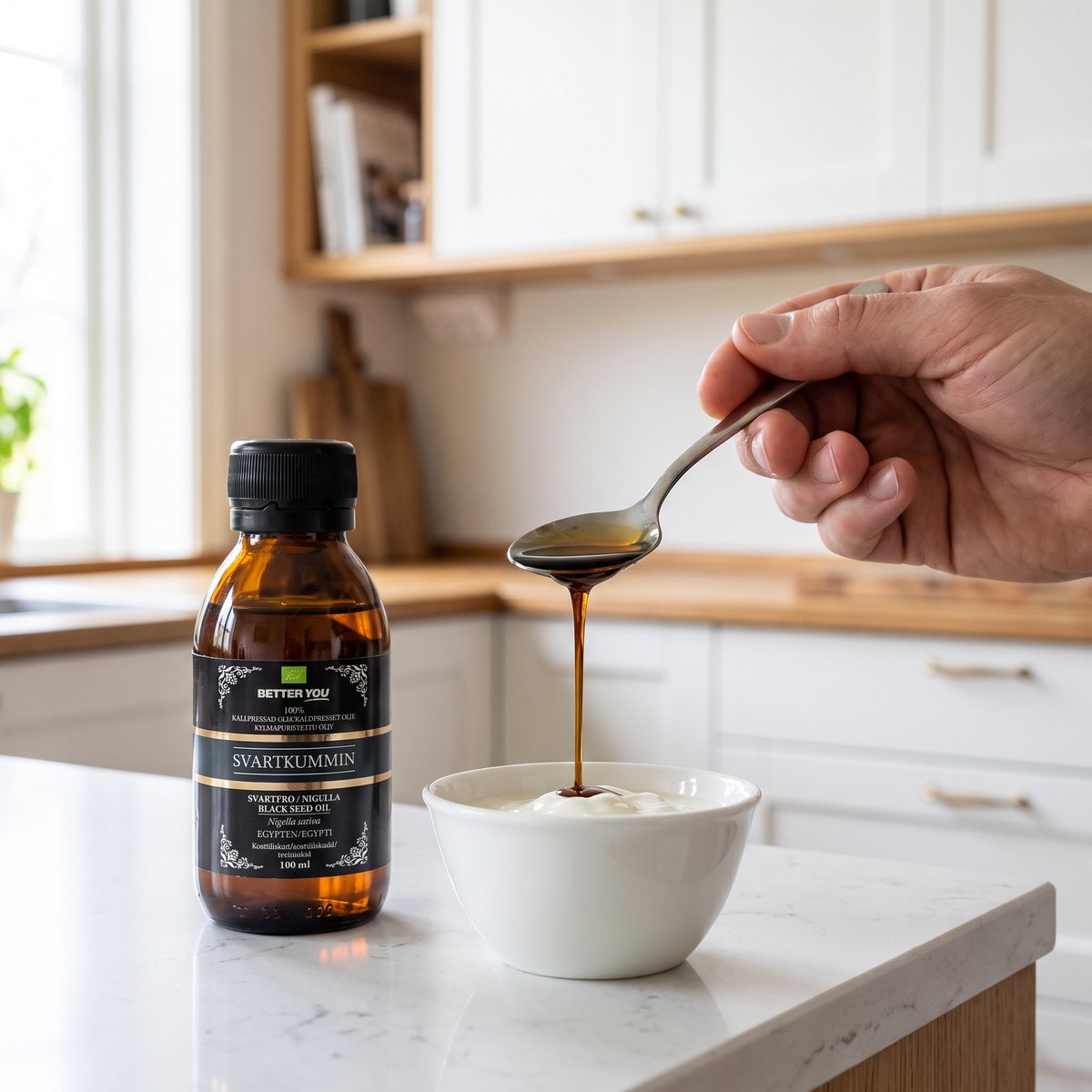 Flaska svartkumminolja i brunt glas på en köksbänk i ett svenskt kök, med en sked som doserar oljan över en skål yoghurt