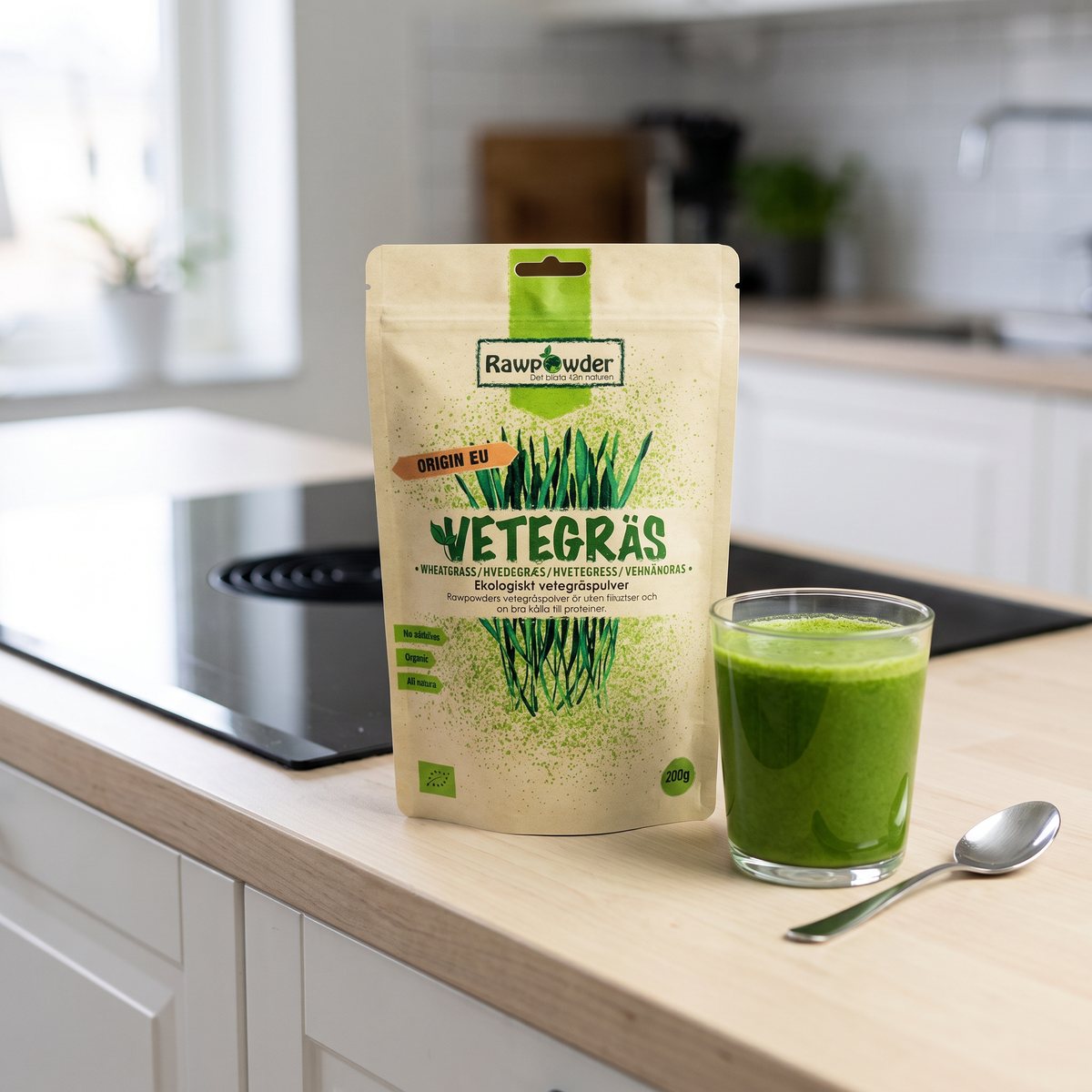 Rawpowders vetegräspåse stående på en köksbänk i björk bredvid ett glas grön vetegräsdrink i ett svenskt kök