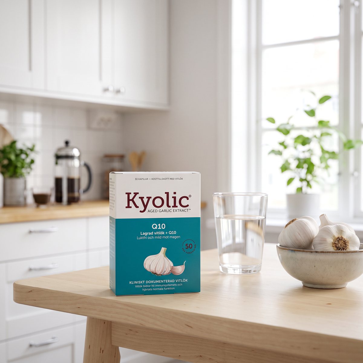 Kartong med Kyolic Original +Q10 på ett björkbord i ett ljust svenskt kök, bredvid ett vattenglas och en skål med vitlök