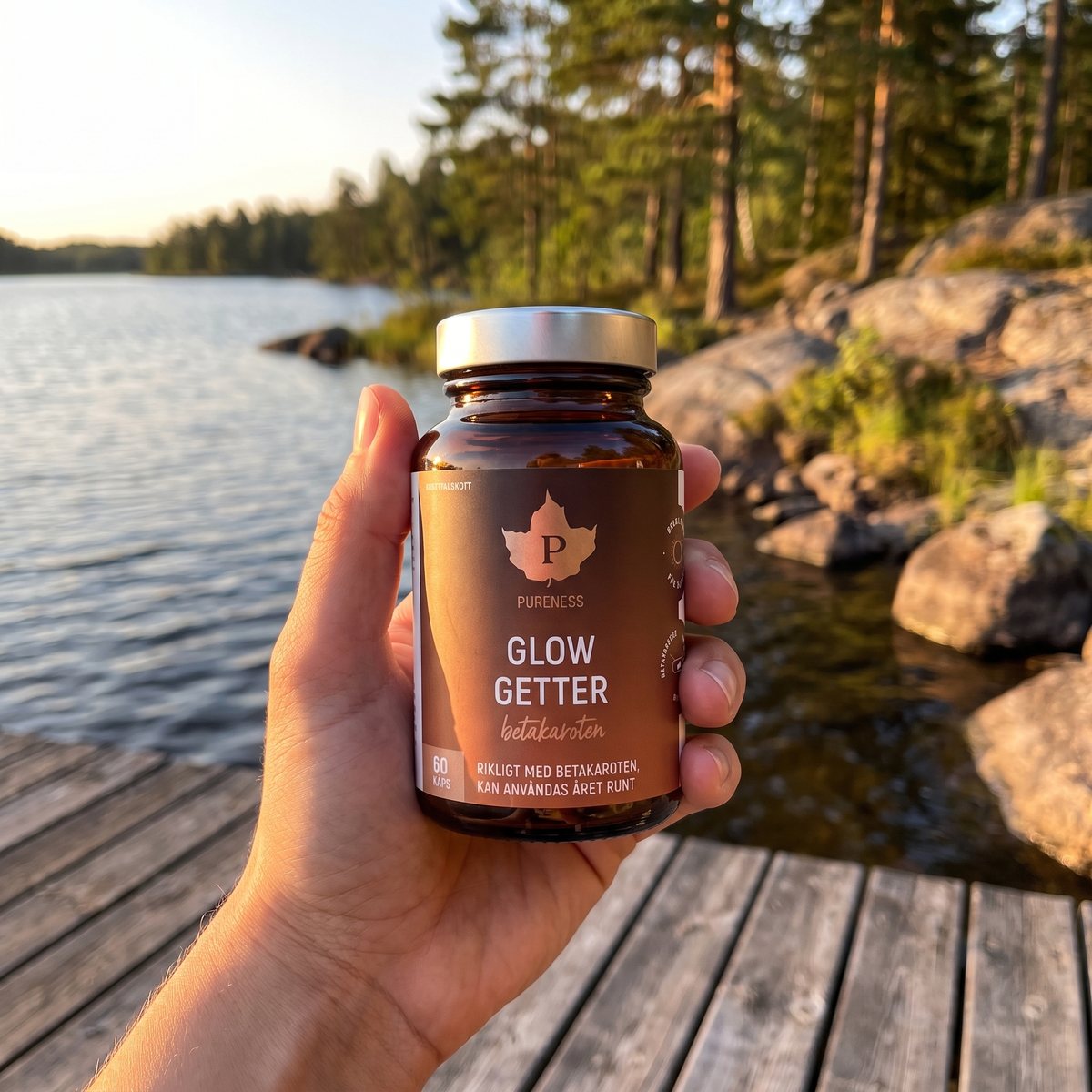 Hand som håller Pureness Glow Getter i brun glasburk på en träbrygga vid en svensk sjö