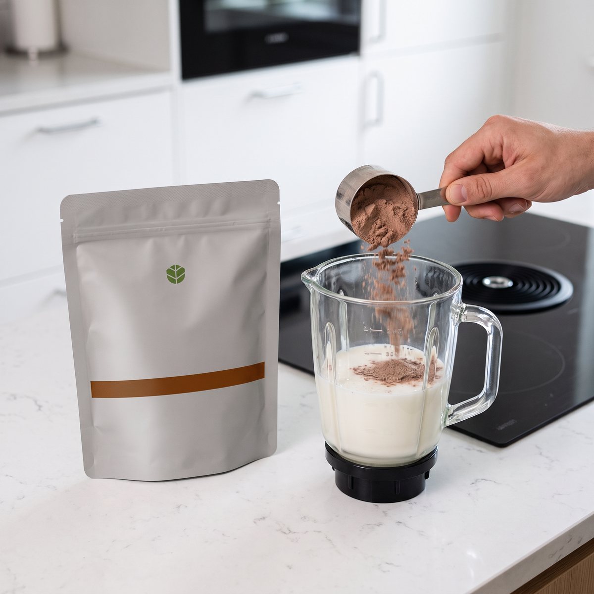 Vitaprana Whey Protein, grå påse med brun rand, som en hand häller chokladpulver i en mixerkanna med mjölk bredvid en induktionshäll i ett svenskt kök