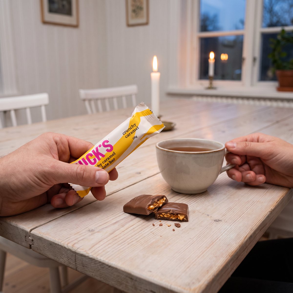 Nicks Crunchy Caramel i handen vid ett matbord med tekopp och en bruten bit med krokant