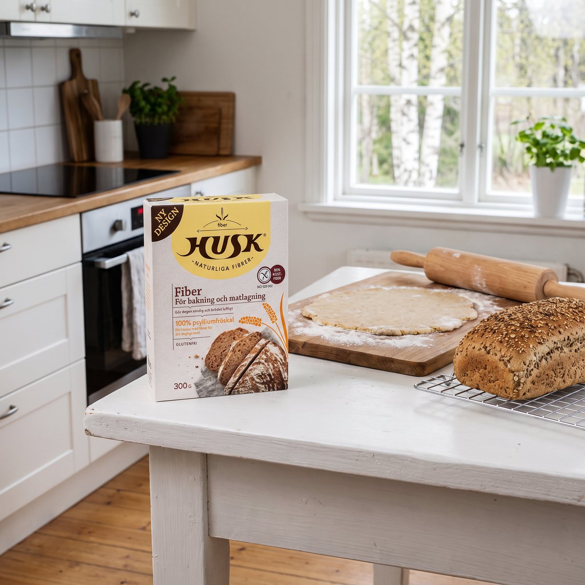 Kartongen FiberHusk på ett vitt köksbord vid utkavlad deg och ett nygräddat bröd i ett svenskt kök
