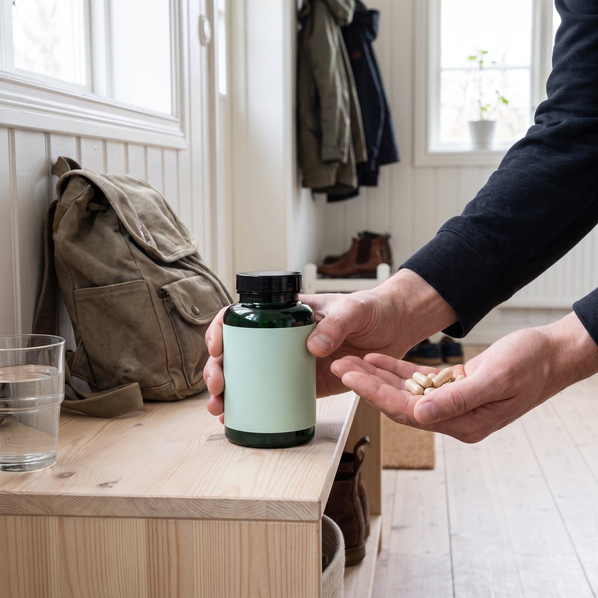Grön glasburk med lecitinkapslar och en hand med kapslar i en svensk hall med ryggsäck