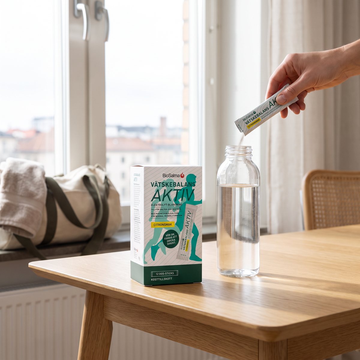 BioSalma Vätskebalans Aktiv: pulver i dospåse hälls i en vattenflaska vid ett köksbord i en svensk lägenhet, gymväska i fönstret.