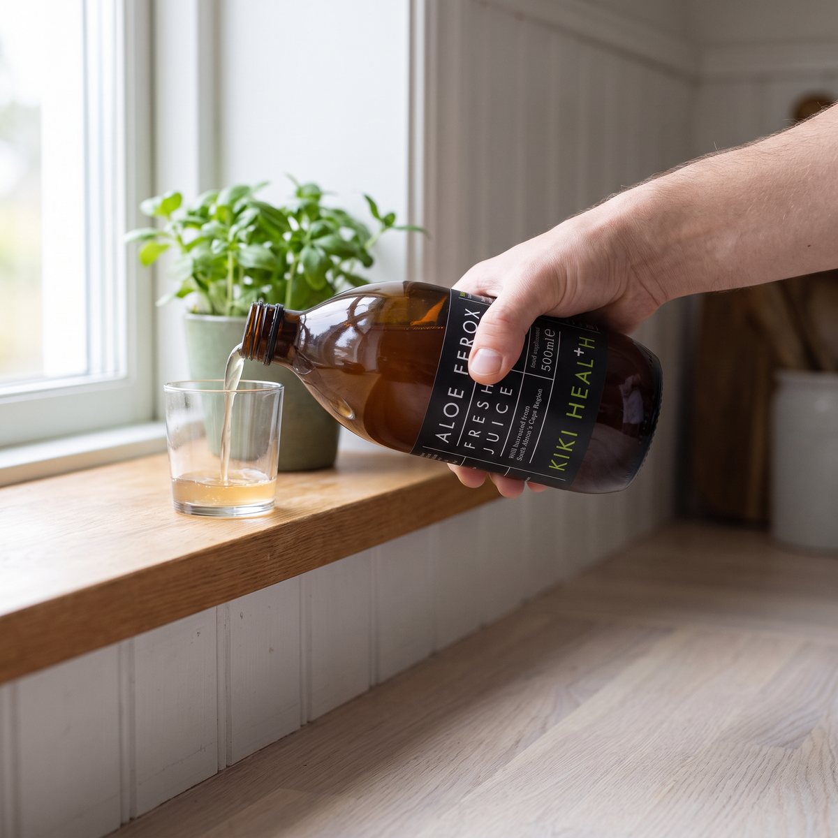 Kiki Health Aloe Ferox Juice, brun glasflaska, hälls upp i ett litet glas i en svensk lägenhet