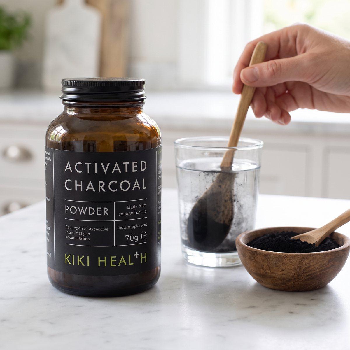 Burk med Kiki Health Activated Charcoal Powder på en marmorbänk i ett svenskt kök, med kolpulver som rörs ut i vatten