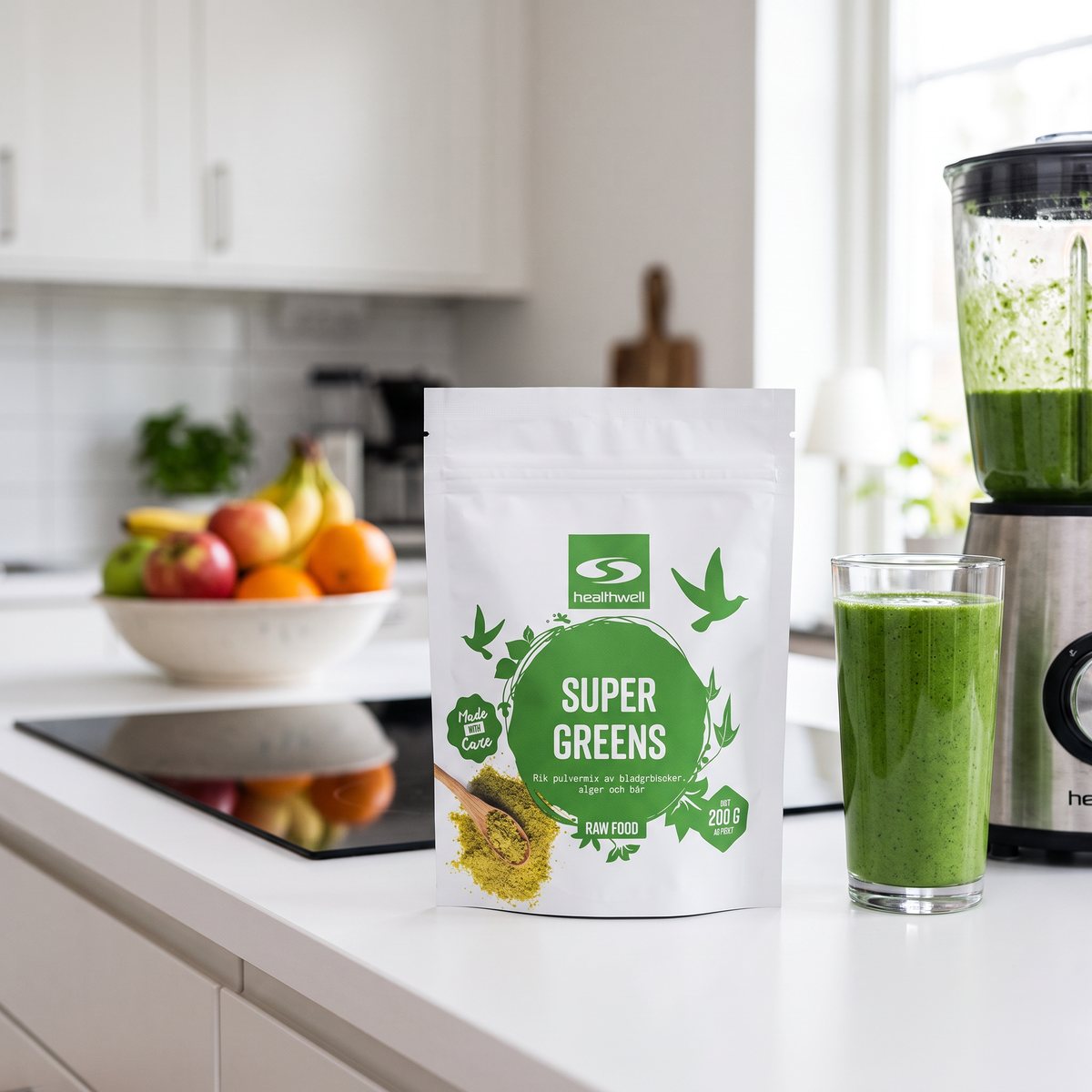 Påse med Healthwell Super Greens bredvid ett glas grön smoothie och en mixer i ett svenskt kök med induktionshäll