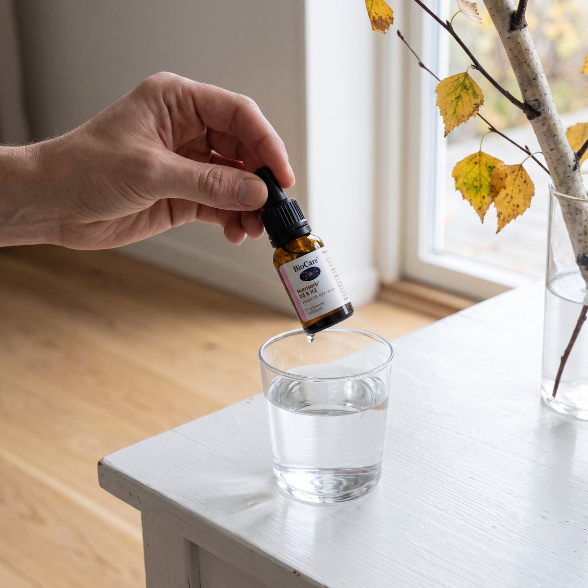 Bärnstensfärgad droppflaska med svart pipett som droppas i ett glas vatten i ett svenskt kök