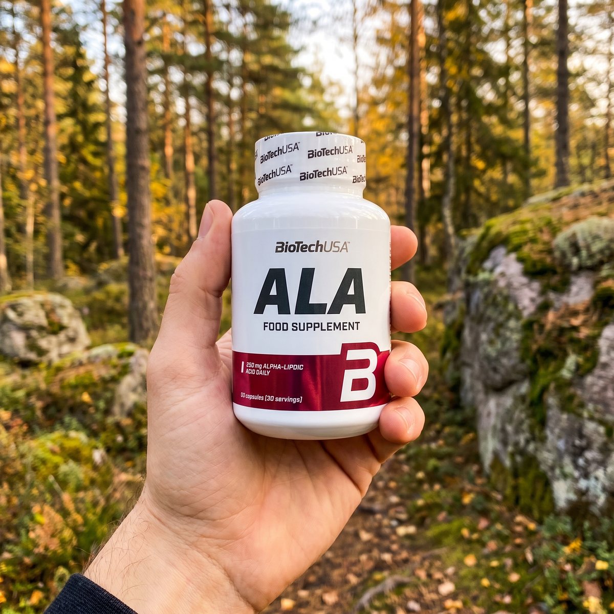 Hand som håller BioTechUSA ALA i en svensk tallskog med granit och höstljus