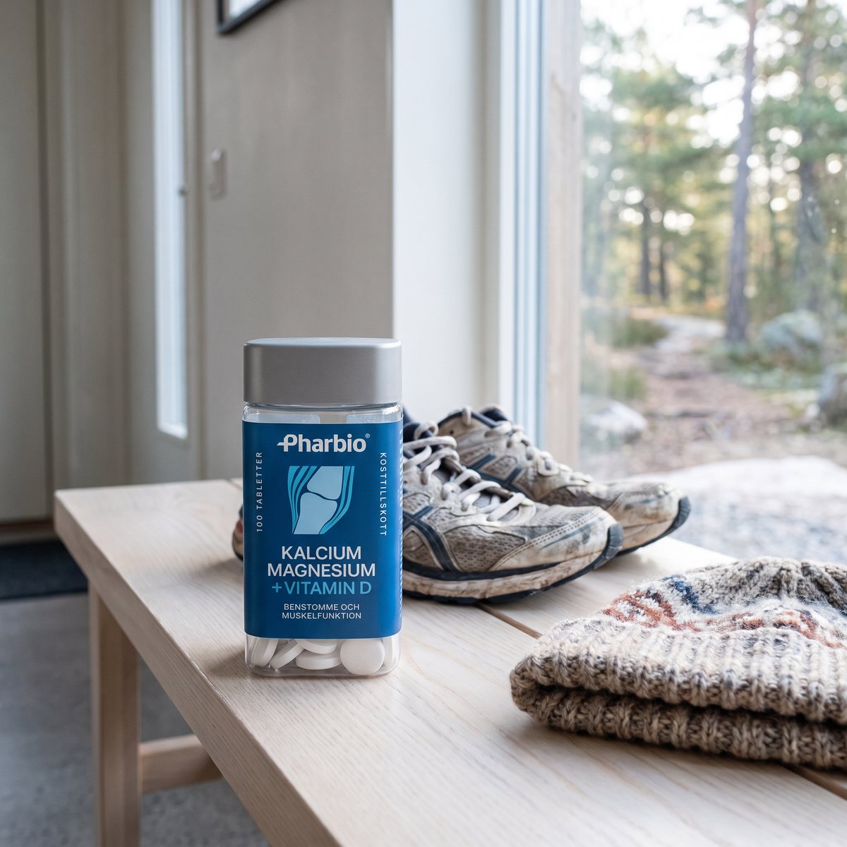 Burk med Pharbio Kalcium, Magnesium + D-vitamin på en träbänk i en svensk hall, med joggingskor och skogsstig utanför