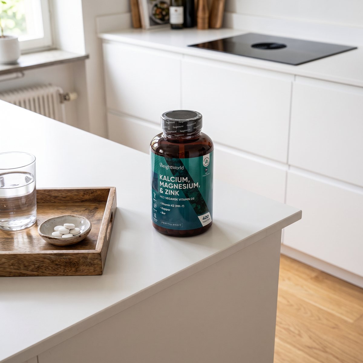 Flaska med WeightWorld Kalcium med magnesium, zink och D3 på en vit köksö i ett svenskt kök, bredvid vatten och några tabletter