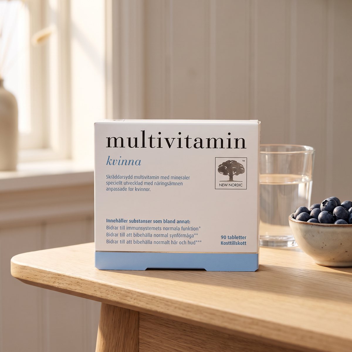 Förpackning New Nordic Multivitamin Kvinna på ett ljust träbord i ett svenskt hem med vattenglas och blåbär