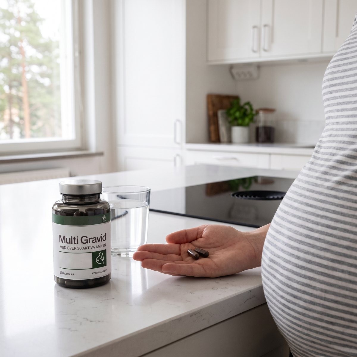 Gravid kvinna i randig tröja med två kapslar i handflatan bredvid burken Elexir Pharma Multi Gravid på en vit köksbänk med induktionshäll