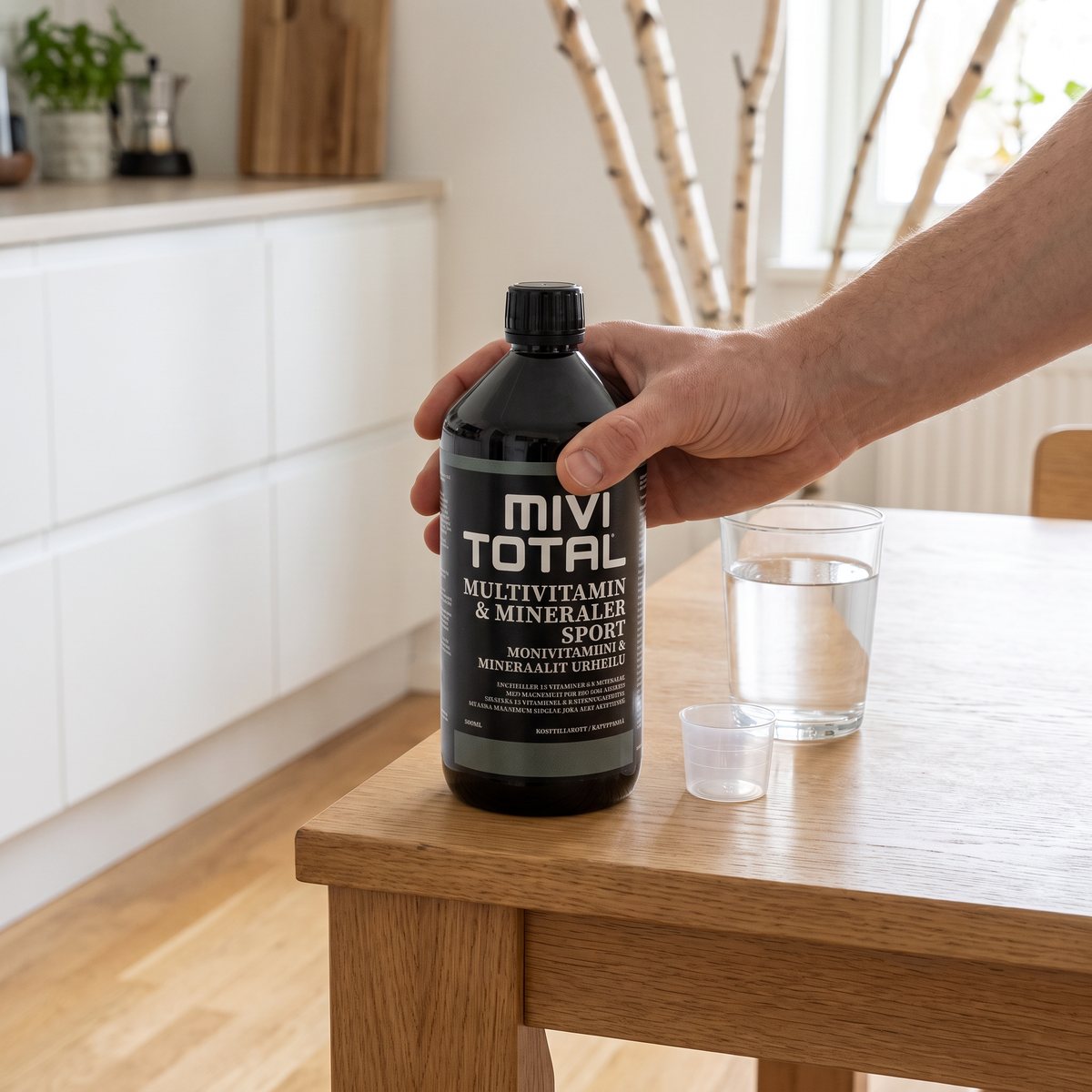 Flaskan Mivitotal Sport på ett köksbord i ett svenskt kök med ett glas vatten och en doseringskopp