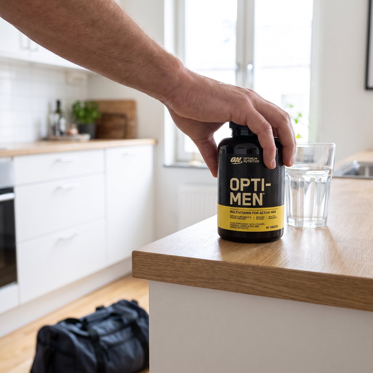 Svart burk Optimum Nutrition Opti-Men hålls i handen vid en köksbänk i ett svenskt kök efter träning