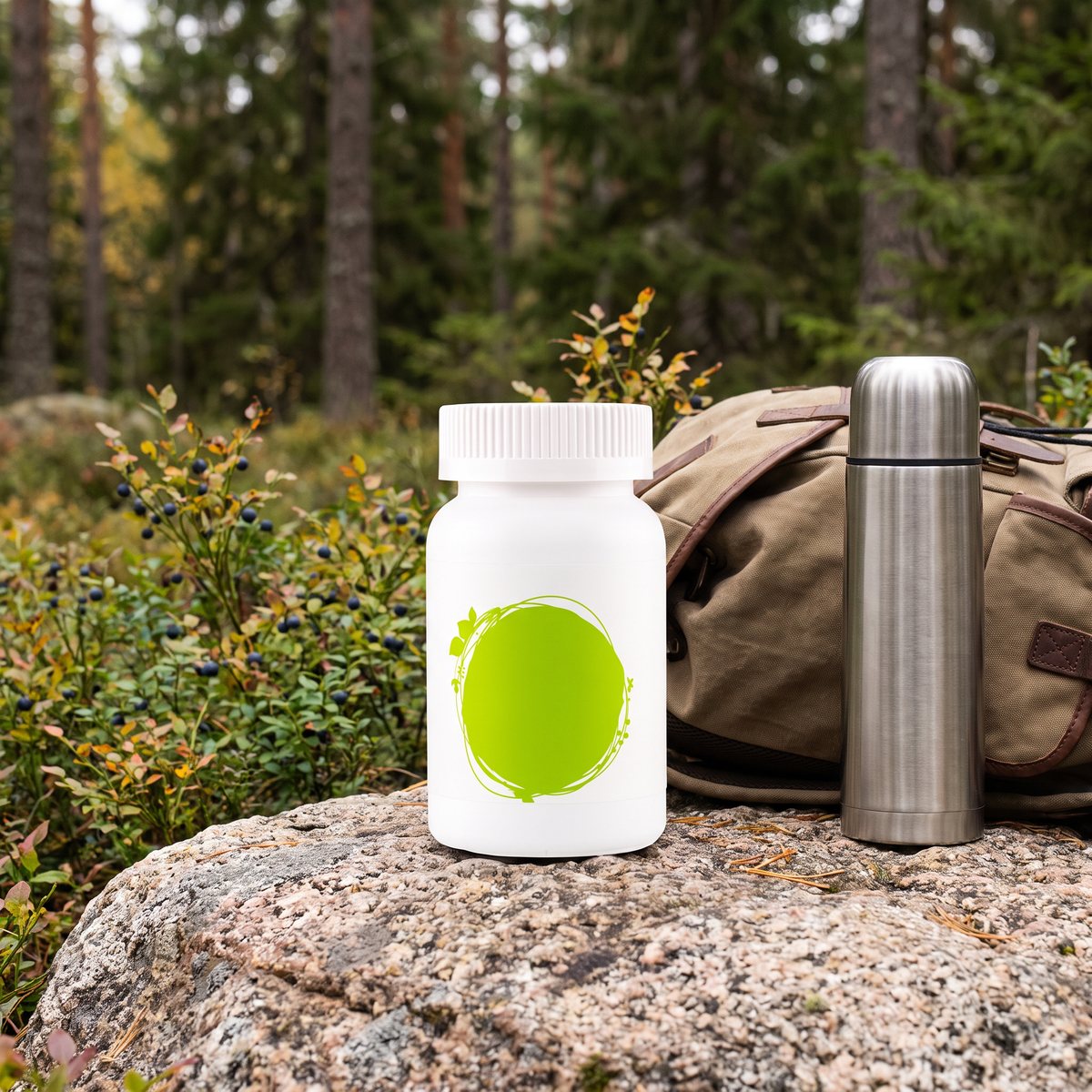 Healthwell Multivitamin Vegan på en granitsten i svensk tallskog med blåbärsris, ryggsäck och termos