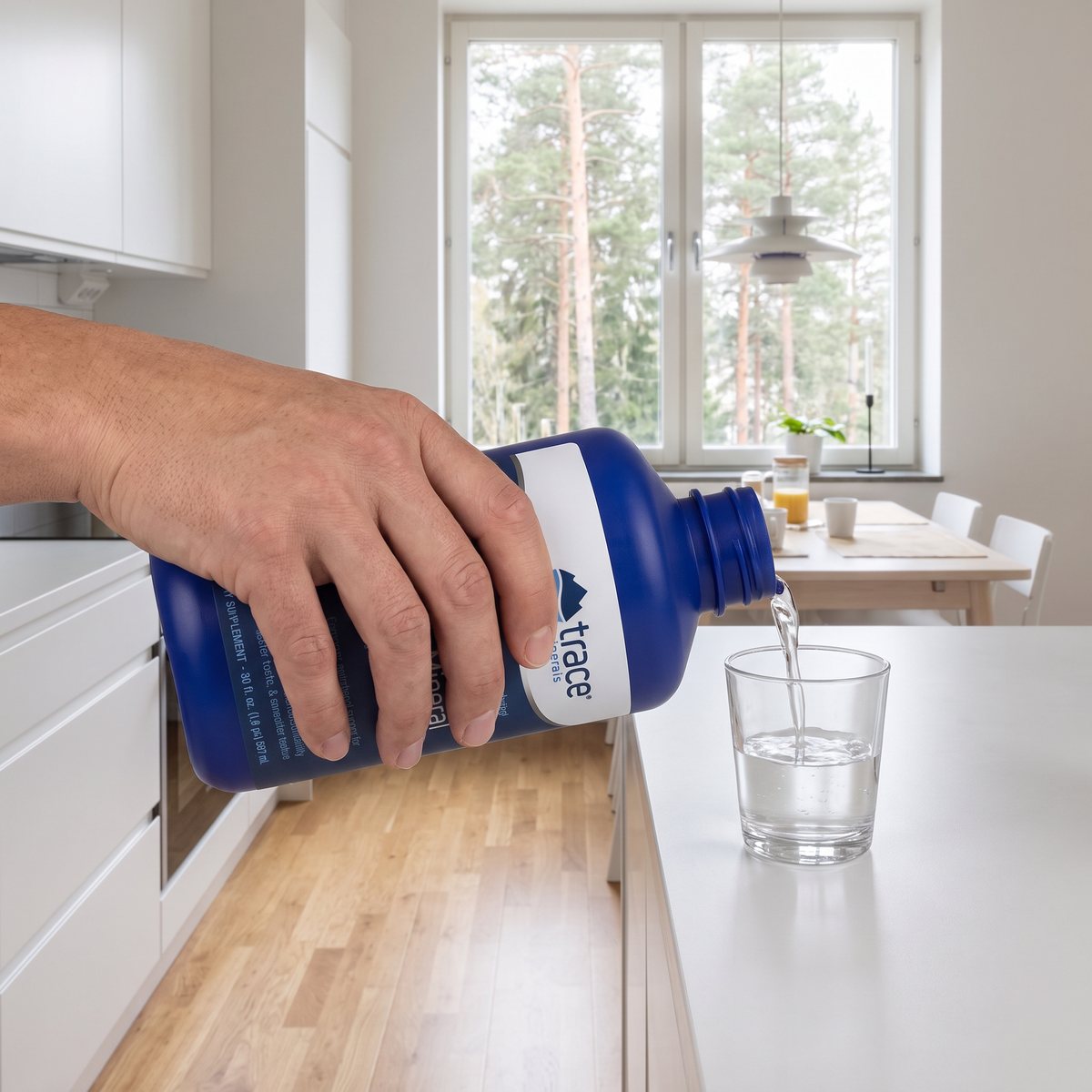 Hand som häller Trace Minerals Liquid Multi Vitamin-Mineral i ett glas på en vit bänk i ett svenskt kök