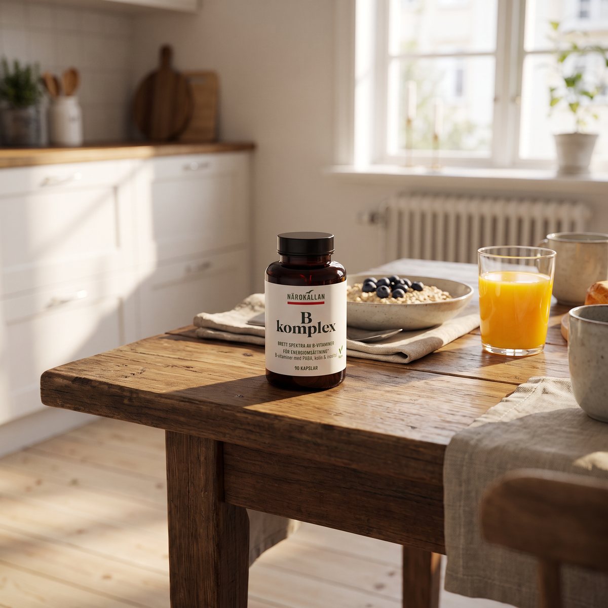 Mörk glasburk med Närokällan B-komplex på ett frukostbord med havregrynsgröt, blåbär och apelsinjuice i ett svenskt kök