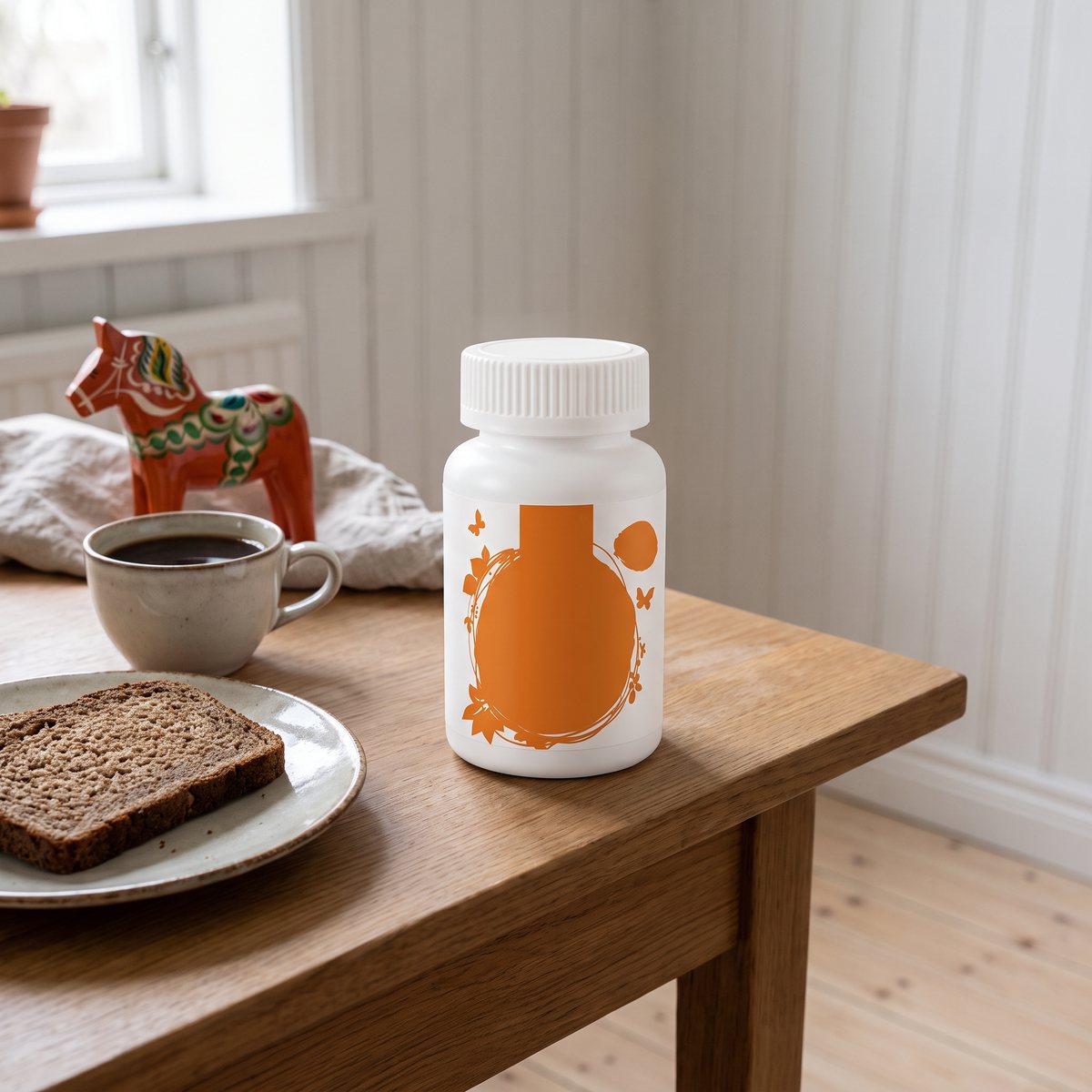 Vit burk med A-vitaminkapslar på ett frukostbord med rågbröd, kaffe och dalahäst i en svensk lägenhet