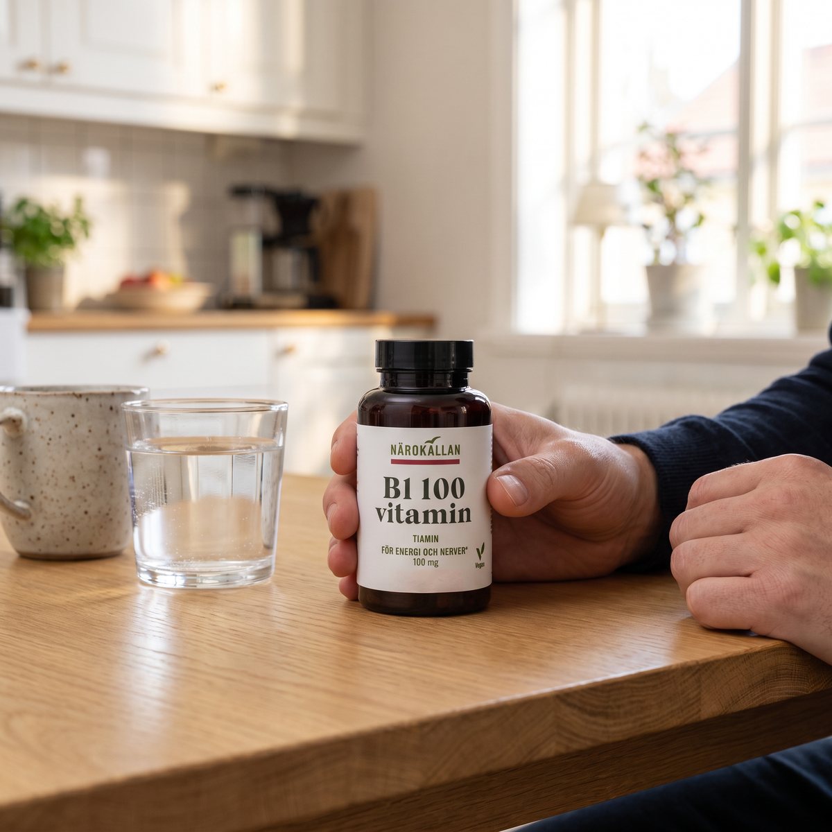 Burk med Närokällan B1 100 mg på ett ljust ekträbord i ett svenskt kök med ett glas vatten och en kopp