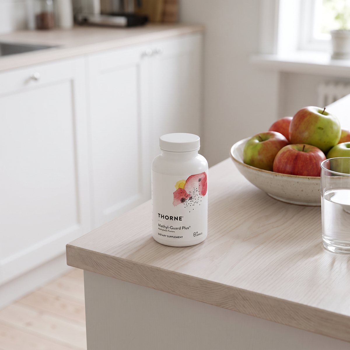 Vit burk med Thorne MethylGuard Plus på en köksbänk bredvid en skål med äpplen i ett svenskt hem