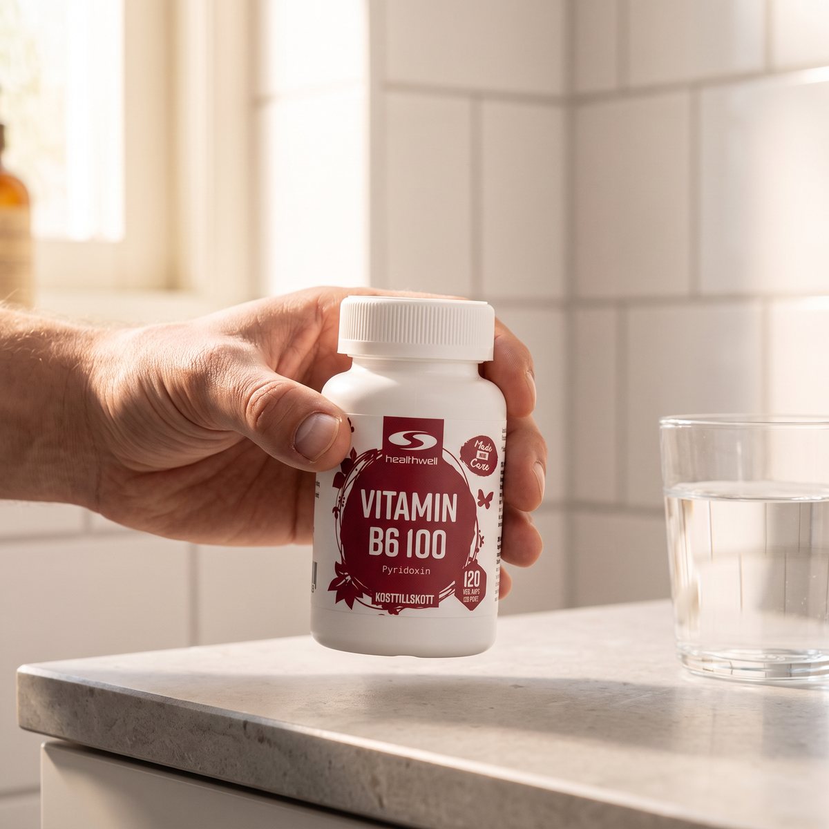 Hand som håller Healthwell Vitamin B6 100 vid en stenbänk i ett svenskt badrum med vita kakelplattor