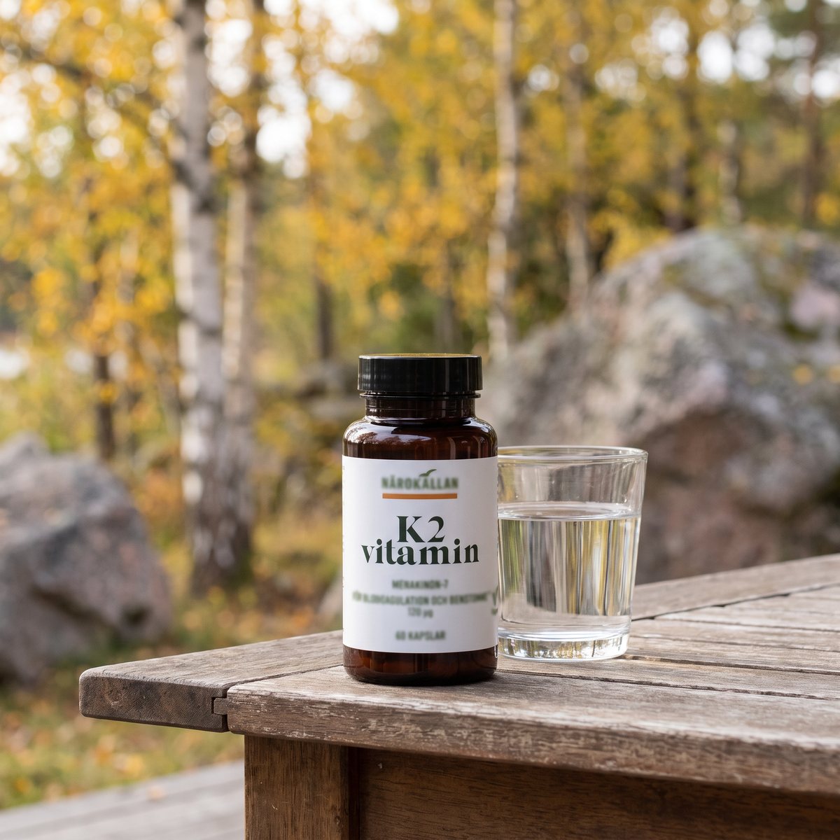 Brun glasburk med K2-vitamin på ett trädgårdsbord på en svensk veranda med björkar