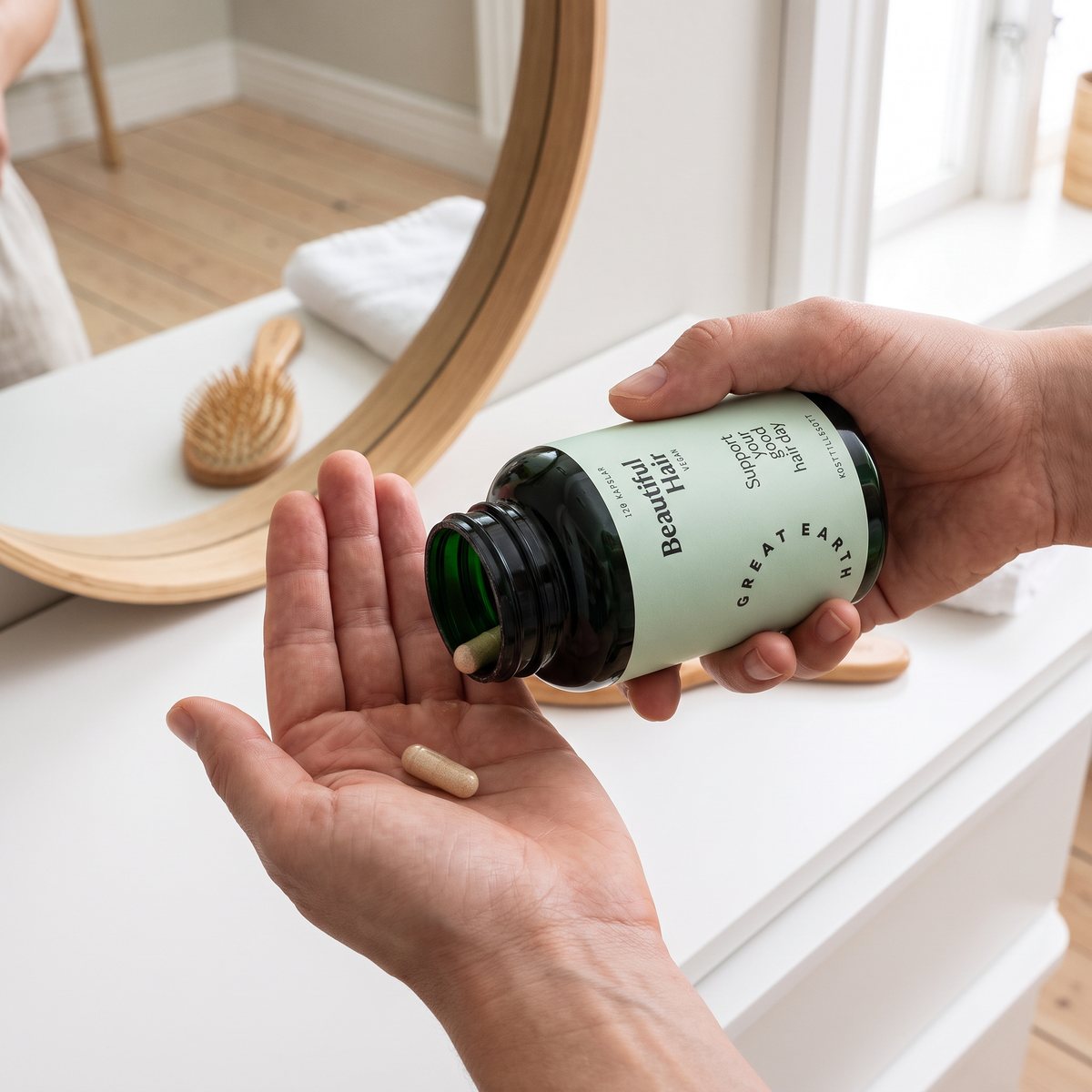 Great Earth Beautiful Hair-burken i en hand som tippar en kapsel i handflatan vid ett badrumsbord i svenskt hem