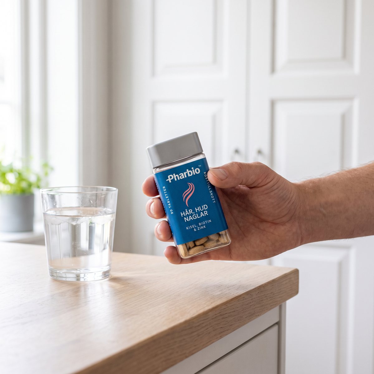 Hand som håller Pharbio Hår, hud & naglar-burken vid en köksbänk i ett svenskt hem